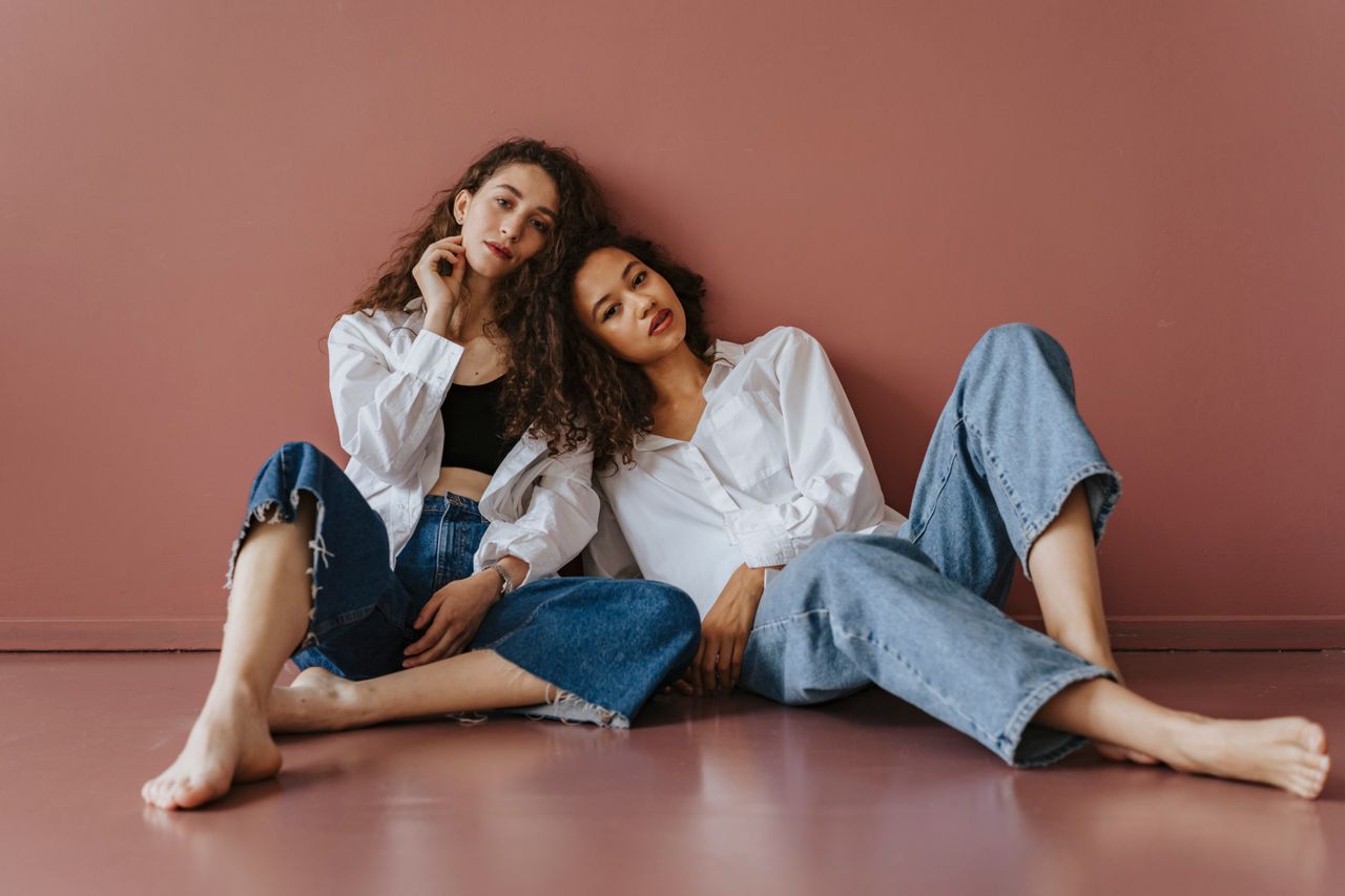 The Art of Drawing Readers In: Your attractive post title goes here Two women sitting against a pink wall, dressed in denim and white shirts, conveying casual elegance.