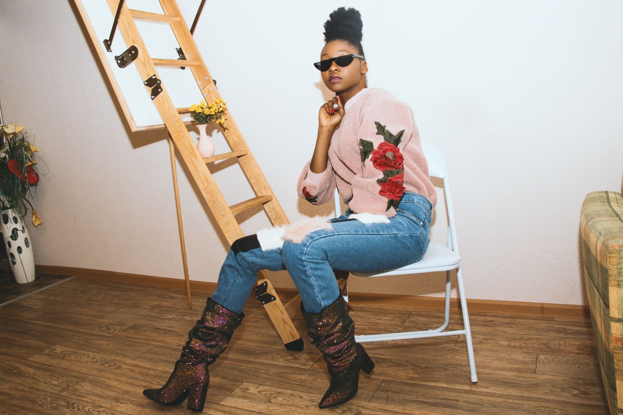 about-us Elegant woman in a chic outfit posing indoors with sunglasses and stylish boots.